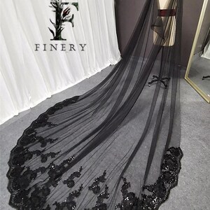May include: Black tulle wedding veil with a scalloped edge and black sequin embroidery. The veil is long and flowing, and it would be a beautiful addition to any wedding.