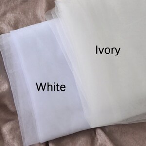 May include: Two swatches of tulle fabric, one white and one ivory. The fabric is soft and sheer, and the colors are subtle.