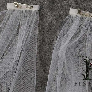 May include: Two white tulle veils with silver clips attached. The veils are made of a soft, sheer fabric and are perfect for adding a touch of elegance to any occasion.