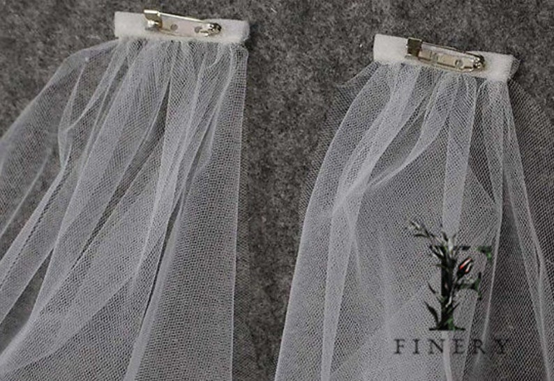 May include: Two white tulle veils with silver clips attached. The veils are made of a soft, sheer fabric and are perfect for adding a touch of elegance to any occasion.