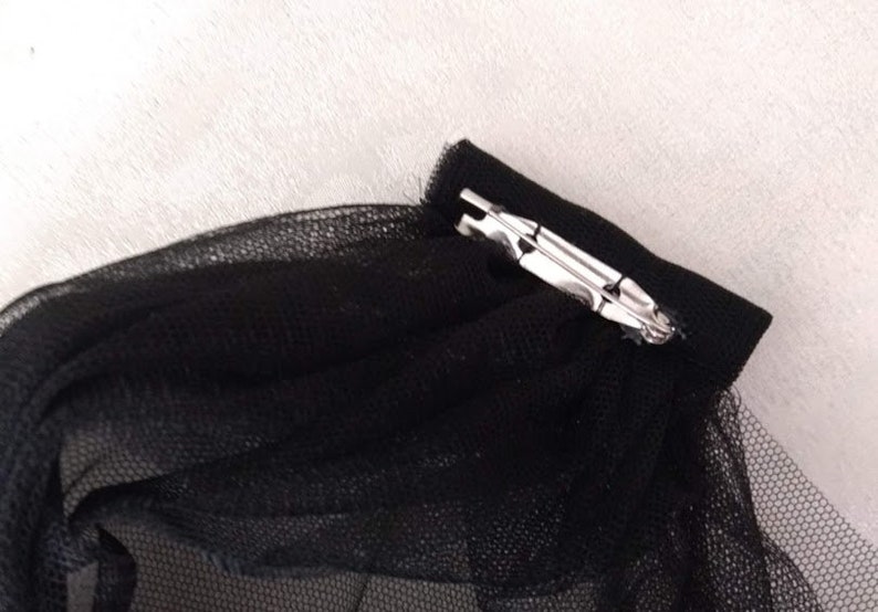 May include: Black tulle fabric with a silver metal clip attached to the edge.