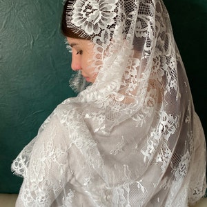 May include: White lace veil with a floral pattern. The veil is delicate and sheer, with a scalloped edge.