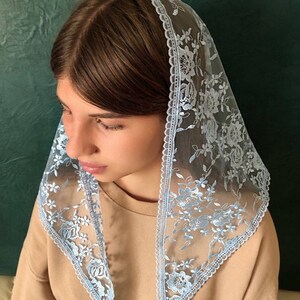 Puede incluir: Un velo de encaje azul claro con bordados florales. El encaje tiene un borde festoneado.