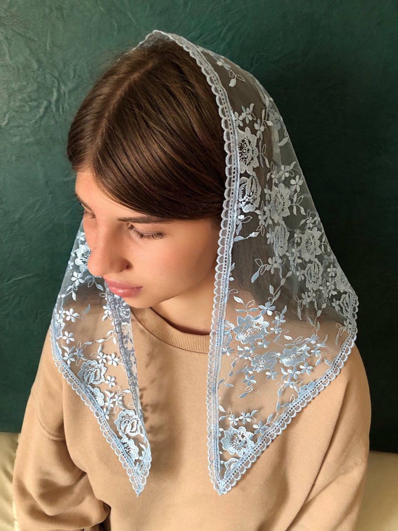 Puede incluir: Un velo de encaje azul claro con bordados florales. El encaje tiene un borde festoneado.