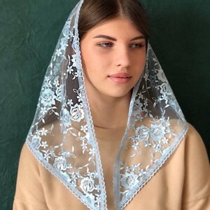 Puede incluir: Un velo de encaje azul claro con bordados florales. El velo est&aacute; doblado en forma triangular y tiene un borde festoneado.