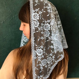 Puede incluir: Un velo de encaje azul claro con un patr&oacute;n floral. El velo est&aacute; adornado con un borde blanco festoneado.