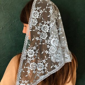 Puede incluir: Un velo de encaje azul claro con un patr&oacute;n floral. El velo est&aacute; adornado con un borde festoneado.