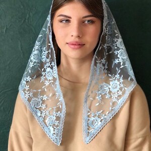 Puede incluir: Un velo de encaje azul claro con bordados florales. El encaje es delicado y tiene un borde festoneado.