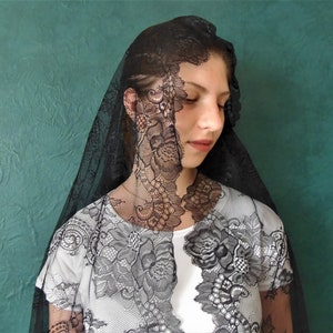 May include: A black lace veil with a floral pattern. The veil is worn over a white shirt.