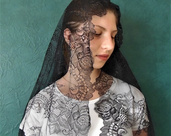 May include: A black lace veil with a floral pattern. The veil is worn over a white shirt.