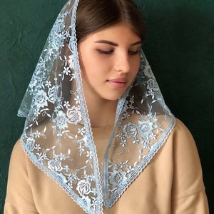 Puede incluir: Un velo de encaje azul claro con bordados florales. El velo est&aacute; doblado en forma triangular y tiene un borde festoneado.