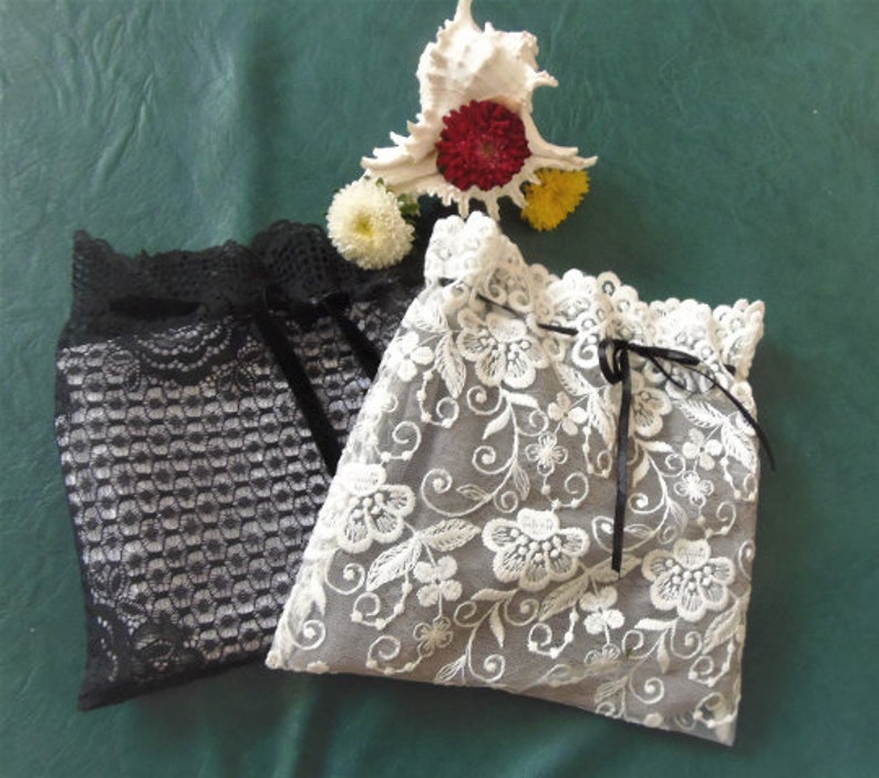 Puede incluir: Dos bolsas delicadas de encaje, una negra y otra blanca con bordados florales. Ambas bolsas tienen un cierre de cord&oacute;n.