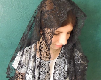 May include: A black lace mantilla with floral embroidery. The mantilla is draped over a person's head and shoulders.