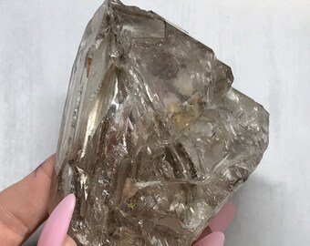 May include: A large, clear quartz crystal with a rough, natural surface. The crystal has a unique, layered appearance with multiple facets. The crystal is translucent and has a slight brown tint.