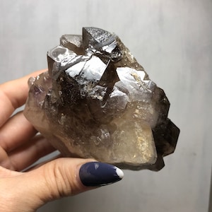 May include: A large, smoky quartz crystal cluster with a natural, raw finish. The crystal is clear with a smoky brown hue and has a pointed, faceted shape.