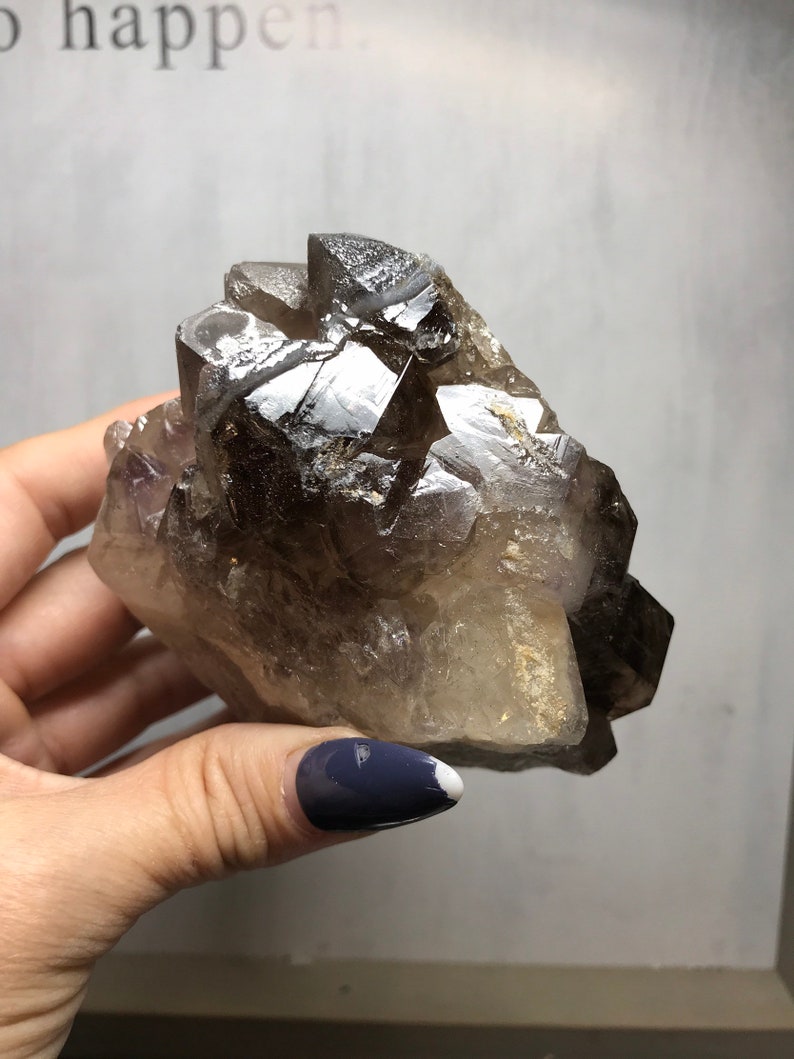 May include: A large, smoky quartz crystal cluster with a natural, raw finish. The crystal is clear with a smoky brown hue and has a pointed, faceted shape.