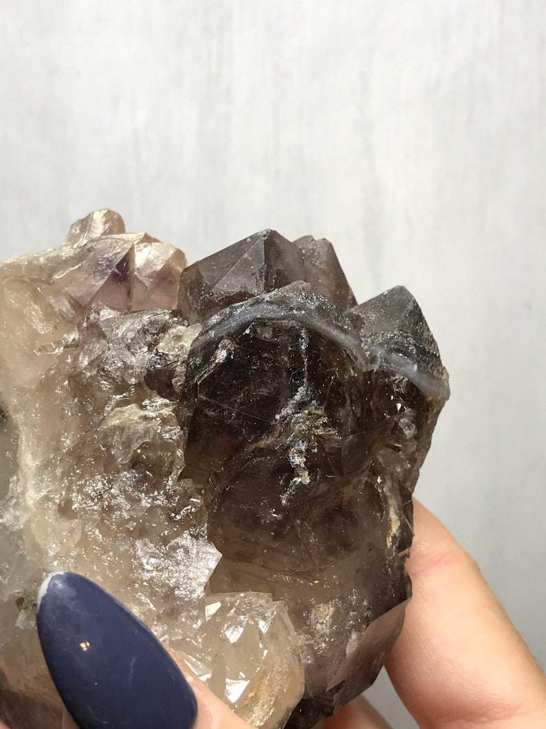 May include: A cluster of smoky quartz crystals with a hint of amethyst. The crystals are clear and have a smoky brown color. The cluster is about 3 inches tall and 2 inches wide.