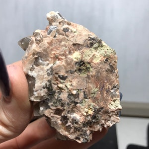 Puede incluir: Un cristal &aacute;spero, gris y marr&oacute;n con una punta de cuarzo transparente. El cristal tiene un aspecto natural y bruto y est&aacute; incrustado en una matriz de roca.