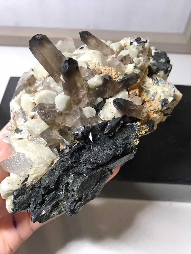 May include: A cluster of smoky quartz crystals with black tourmaline crystals on a matrix of white quartz. The crystals are arranged in a random pattern and have a variety of sizes and shapes.