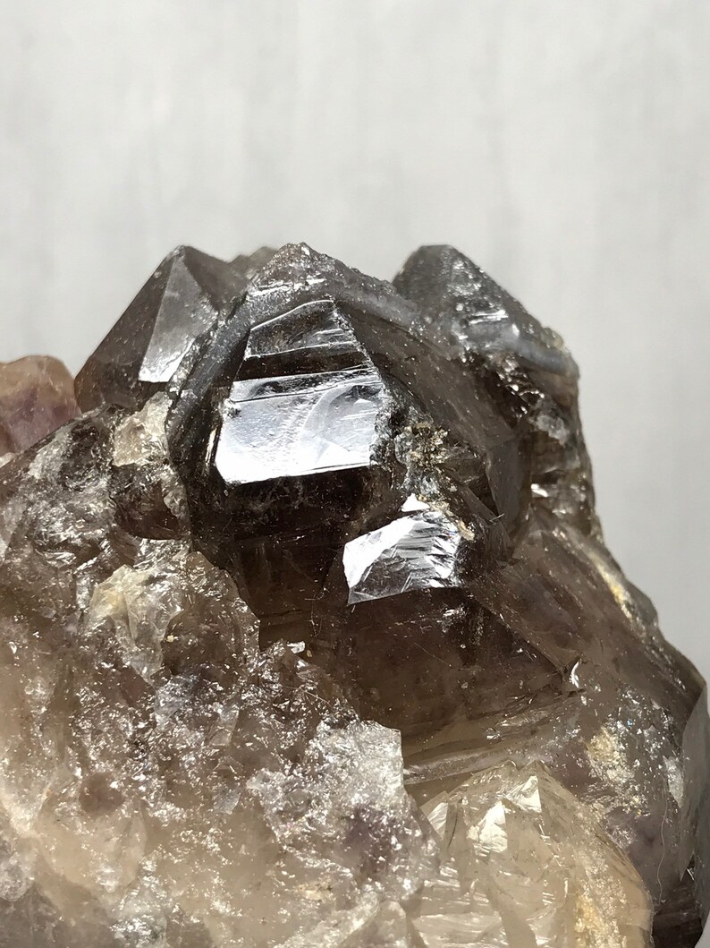 May include: A cluster of smoky quartz crystals with a dark, almost black, hue. The crystals are clustered together in a natural formation, showcasing their unique facets and textures.