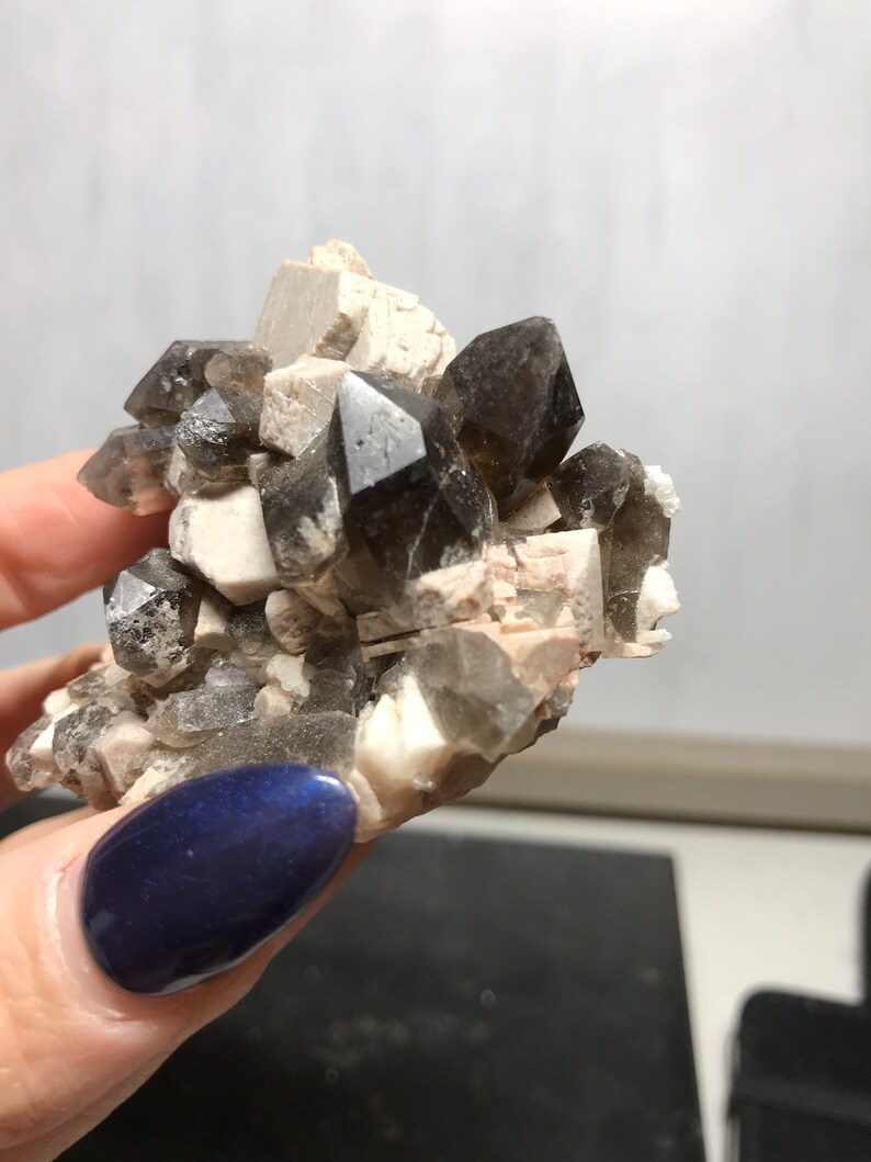 Puede incluir: Un c&uacute;mulo de cristales de cuarzo ahumado con una matriz blanca. Los cristales son transl&uacute;cidos y tienen un color marr&oacute;n oscuro.