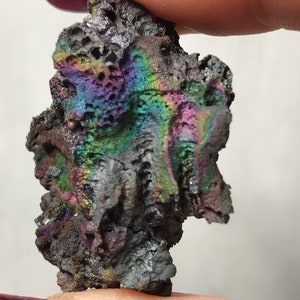 Pu&ograve; includere: Un piccolo sasso grigio e nero iridescente con una superficie ruvida e testurizzata. La pietra ha un bagliore arcobaleno.