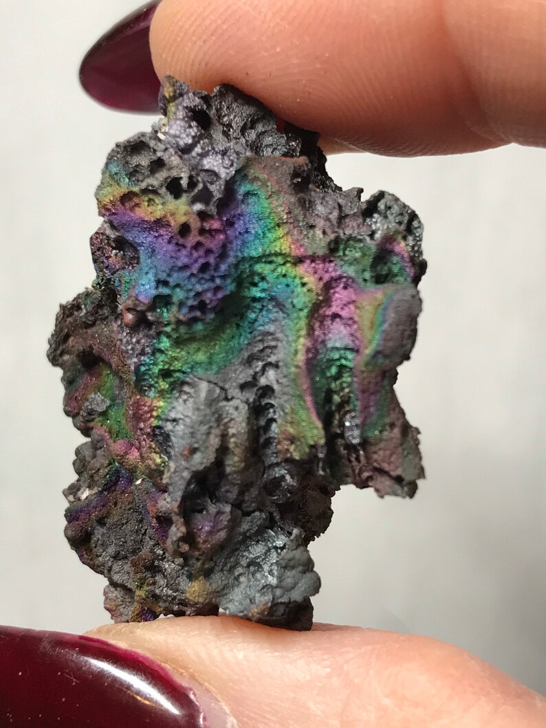 Pu&ograve; includere: Un piccolo sasso grigio e nero iridescente con una superficie ruvida e testurizzata. La pietra ha un bagliore arcobaleno.