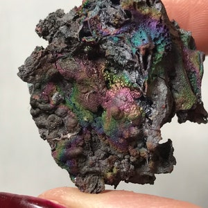 Pu&ograve; includere: Un pezzo di goethite iridescente, nero e grigio con una superficie ruvida e testurizzata. La goethite ha un bagliore arcobaleno.