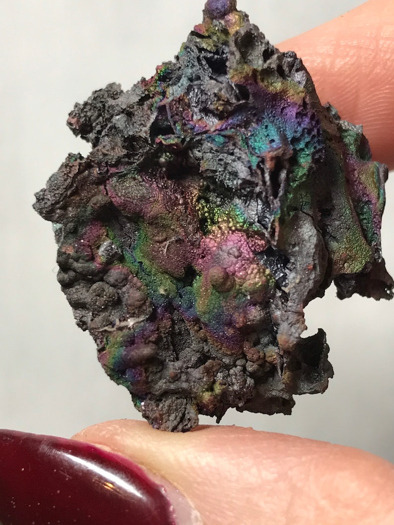 Pu&ograve; includere: Un pezzo di goethite iridescente, nero e grigio con una superficie ruvida e testurizzata. La goethite ha un bagliore arcobaleno.