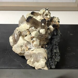May include: A cluster of smoky quartz crystals with clear quartz crystals and black mineral matrix.