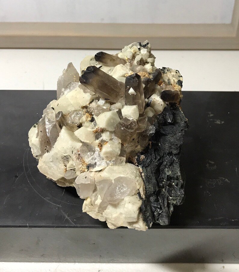 May include: A cluster of smoky quartz crystals with clear quartz crystals and black mineral matrix.