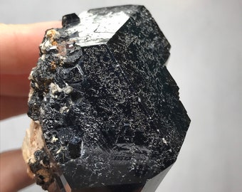 May include: A black, faceted, and highly polished crystal with a rough, brown, and white matrix. The crystal is a dark, opaque black and has a sharp, geometric shape.