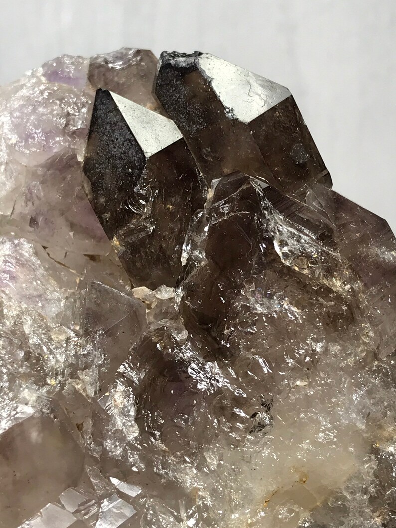 May include: A cluster of smoky quartz crystals with a few amethyst crystals. The smoky quartz crystals are clear and have a dark gray color. The amethyst crystals are purple and have a translucent appearance.
