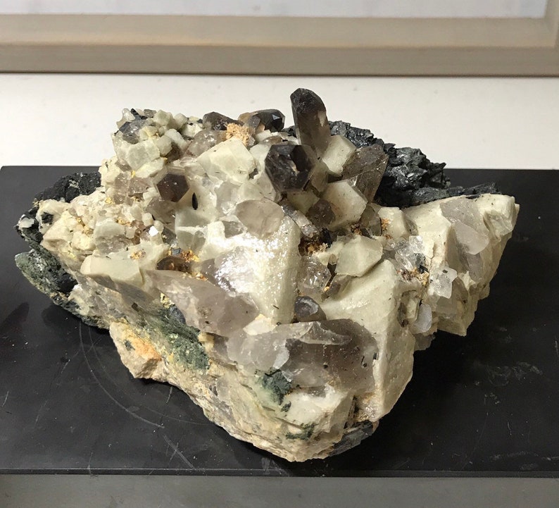 May include: A cluster of smoky quartz crystals embedded in a matrix of white and gray rock. The crystals are translucent and have a smoky brown color. The rock is rough and textured.