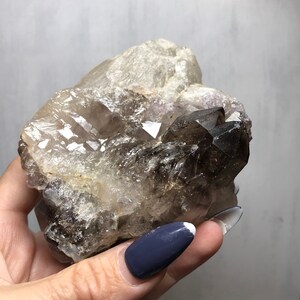 May include: A large, clear quartz crystal with smoky quartz inclusions. The crystal has a natural, rough texture and is a beautiful example of the mineral.