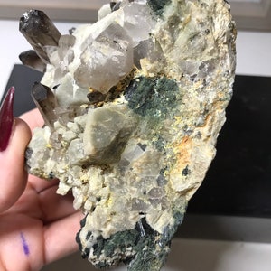 May include: A cluster of smoky quartz crystals embedded in a matrix of white and green rock. The crystals are clear and have a smoky brown color. The matrix is covered in green moss.