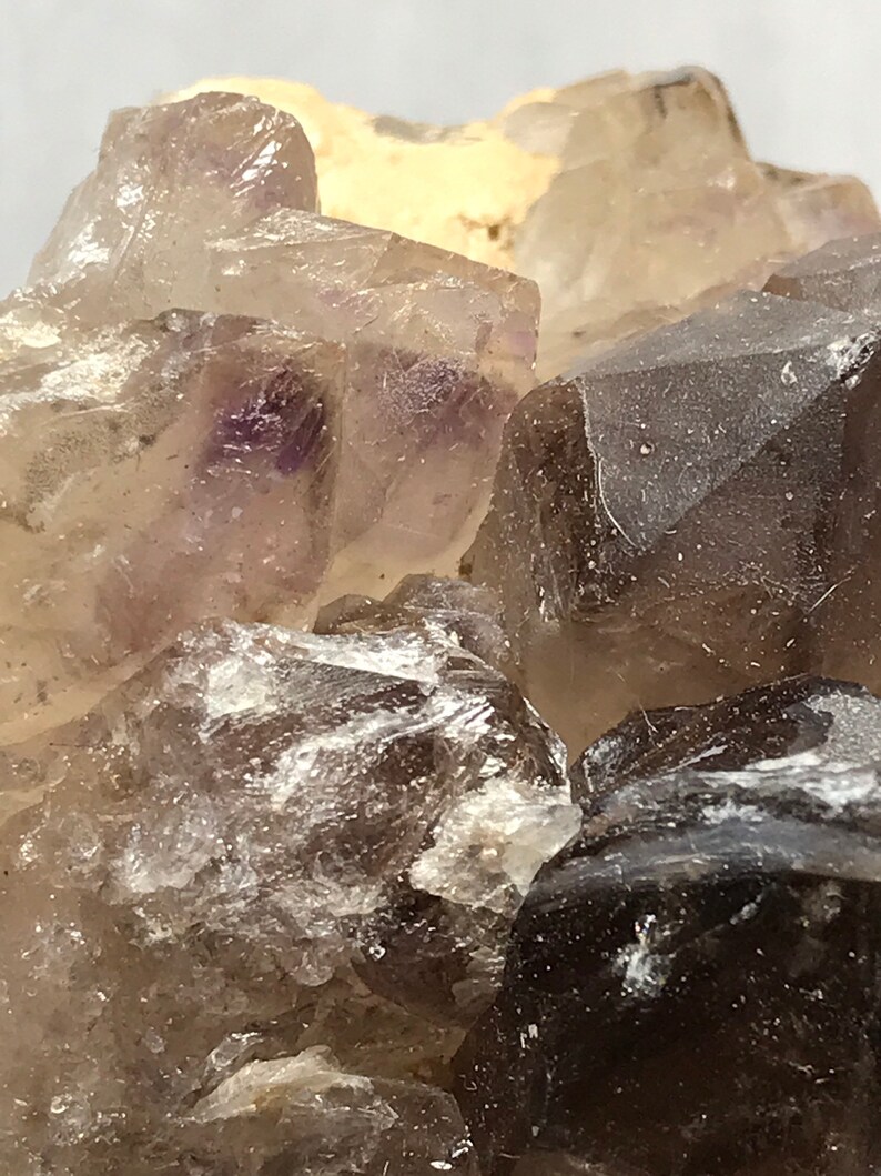 May include: Close-up of a cluster of smoky quartz crystals with a hint of purple. The crystals are translucent and have a rough, natural texture.