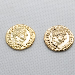 Op de afbeelding: Twee goudkleurige replica's van Romeinse munten met reliëfletters en een profielbeeld van een persoon aan elke kant.