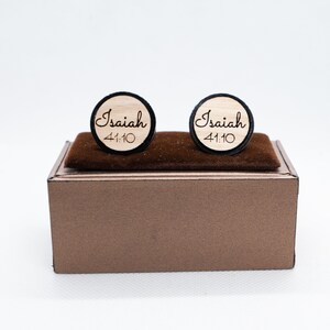 May include: A pair of wooden cufflinks with a black border. The cufflinks are engraved with the text "Isaiah 41:10".