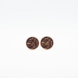 Puede incluir: Un par de gemelos hechos de dos monedas de color cobre. Cada moneda presenta un diseño de pájaro.