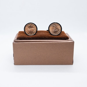 May include: A pair of gold cufflinks with a brown box. The cufflinks feature a design of a falcon and the text "United Arab Emirates".