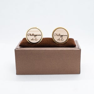 May include: Two gold cufflinks with a wooden inlay. The cufflinks are engraved with the text "Philippians 4:6".