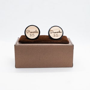 May include: A pair of wooden cufflinks with a black border. The cufflinks are engraved with the text "Proverbs 3:5". The cufflinks are displayed in a brown box.
