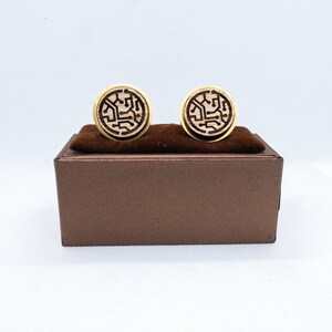 May include: A pair of gold cufflinks with a wood inlay featuring a circuit board design. The cufflinks are displayed in a brown box.
