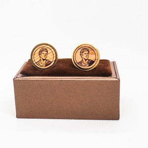 Op de afbeelding: Een paar houten manchetknopen met gouden accenten, met een portret van een man in een doos.