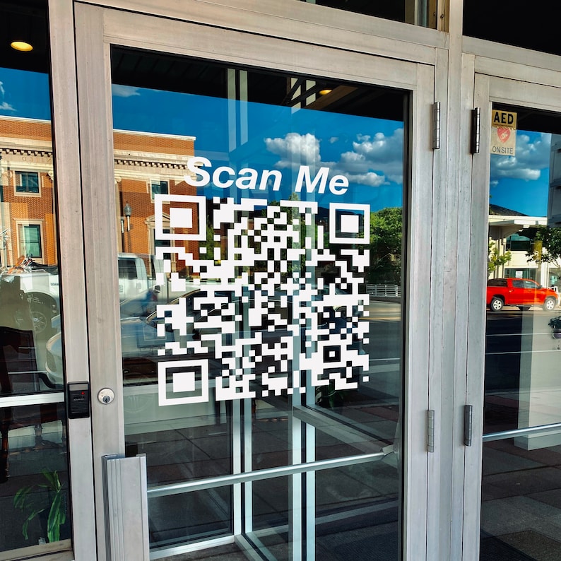 Peut inclure: Porte vitr&eacute;e avec un grand code QR blanc et les mots "Scan Me". La porte refl&egrave;te un ciel bleu avec des nuages et l'ext&eacute;rieur d'un b&acirc;timent. Le cadre de la porte est argent&eacute;.
