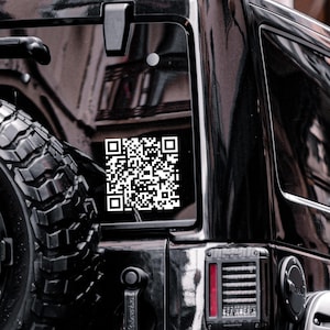 Peut inclure: Un autocollant de code QR blanc est appos&eacute; sur la vitre arri&egrave;re d'un v&eacute;hicule noir. L'autocollant est rectangulaire et pr&eacute;sente un motif complexe de carr&eacute;s noirs et blancs. Le pneu et le feu arri&egrave;re du v&eacute;hicule sont &eacute;galement visibles.