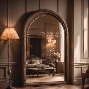 May include: An ornate, arched mirror with a white inscription that reads "Please find your seat. Welcome to our Wedding. Ashley & Kaden 4/27/23".