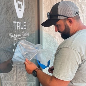 Person installing their custom vinyl decal on a glass door.