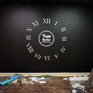 Puede incluir: Una pared negra con una esfera de reloj blanca pintada en ella. La esfera del reloj tiene n&uacute;meros romanos y las palabras "Time Master Escape Rooms" en un c&iacute;rculo en el centro.